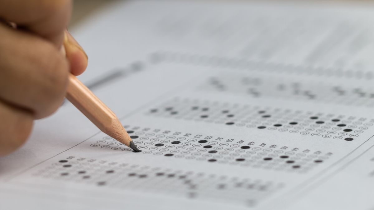 A close-up of a hand with a pencil filling in test answer sheet bubbles.
