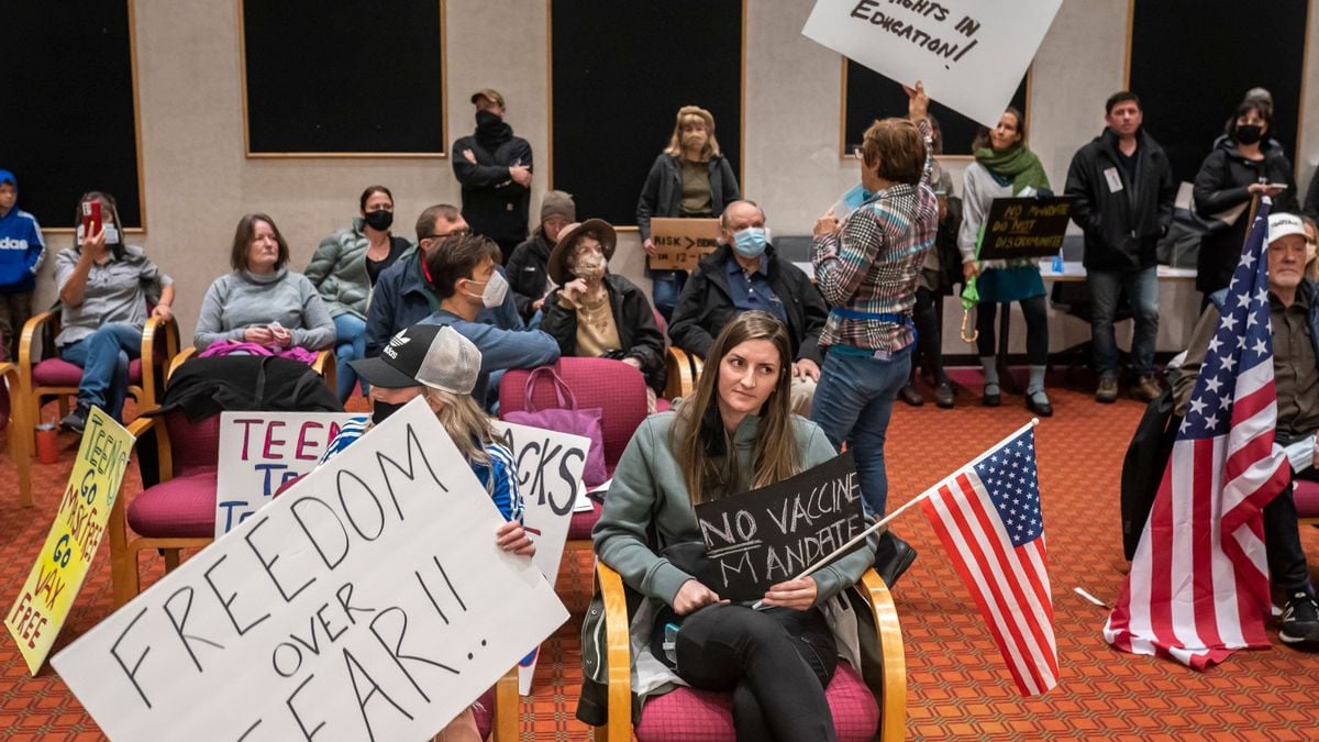 Parents holding signs and American flags attend a school board meeting