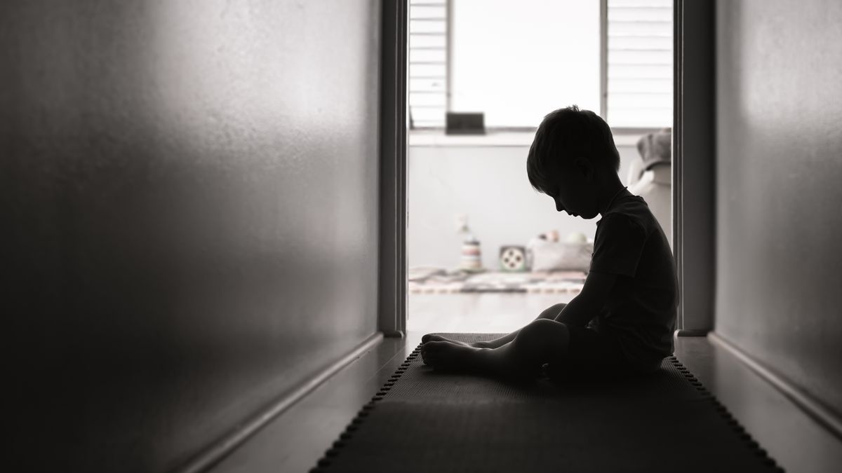 A silhouette of a young child sitting on the floor of a hallway in a home.