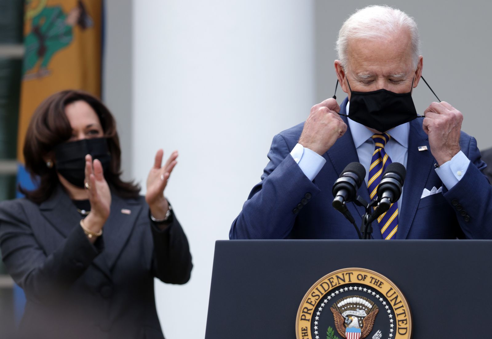 President Joe Biden takes off his mask as Vice President Kamala Harris looks on during an event on the American Rescue Plan in the Rose Garden of the White House on March 12, 2021