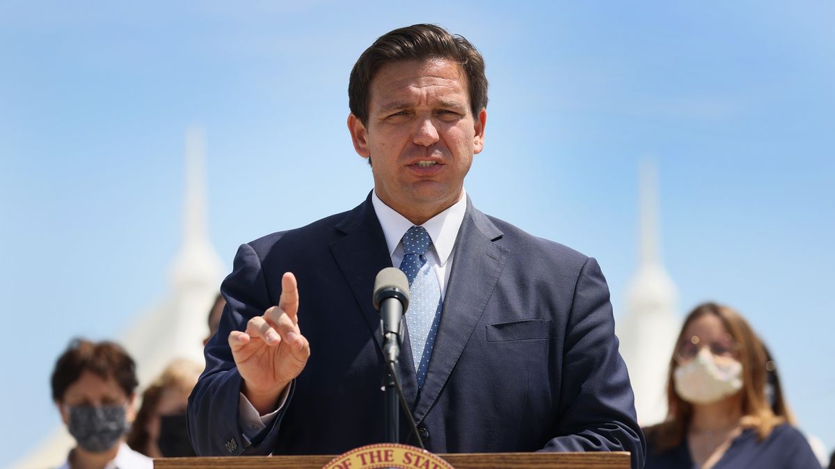Florida Gov. Ron DeSantis speaks at a podium with two masked people behind him.