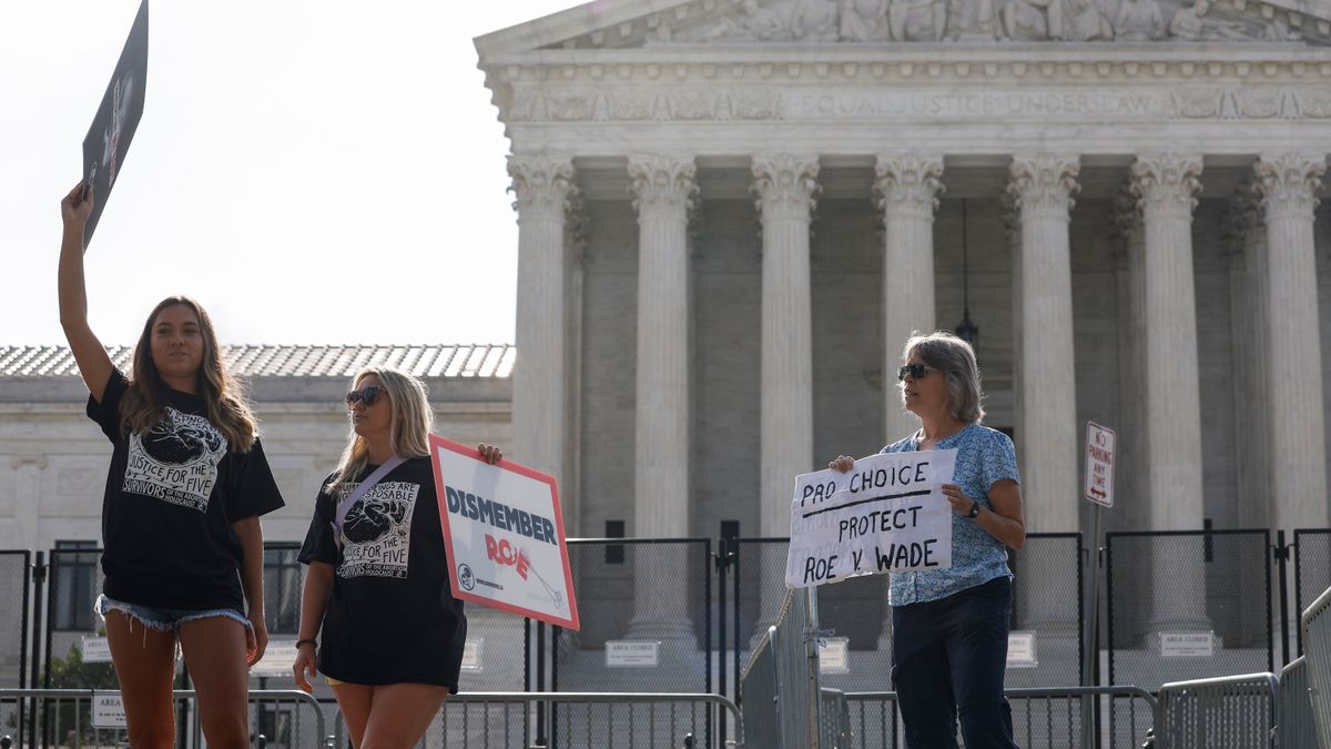 An abortion rights activist stands next to anti-abortion rights activists in front of the U.S. Supreme Court Building, which is surrounded by fencing.