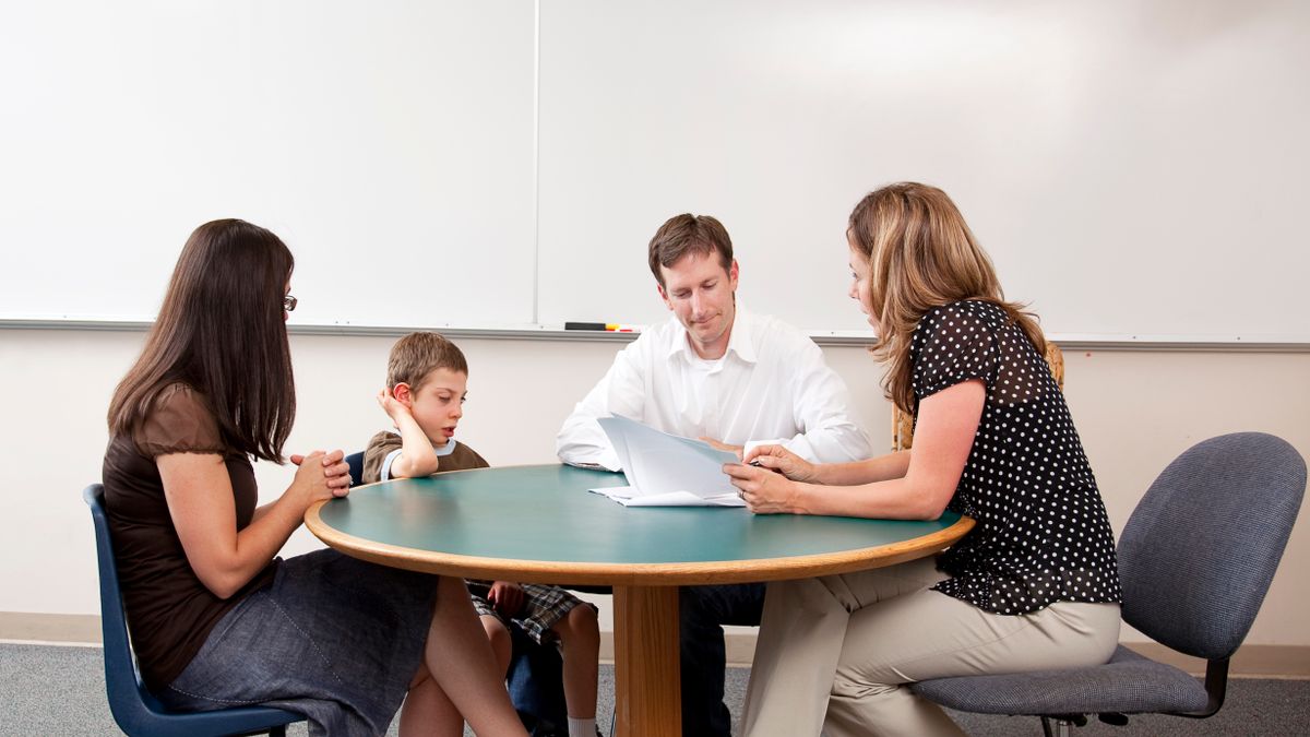 Two parents and their child sit with a teacher to discuss the student's performance.