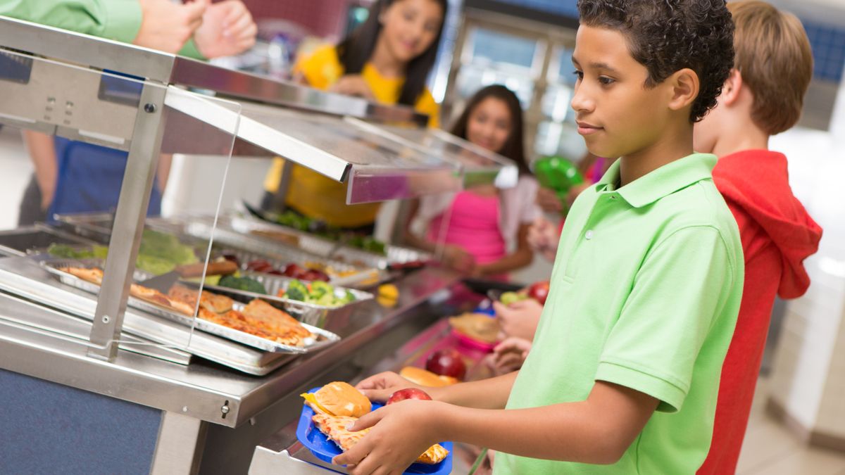 A student walks away from the cafeteria line while holding a tray of food.
