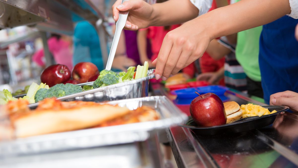 Cafeteria worker helping elementary students select food in lunch line