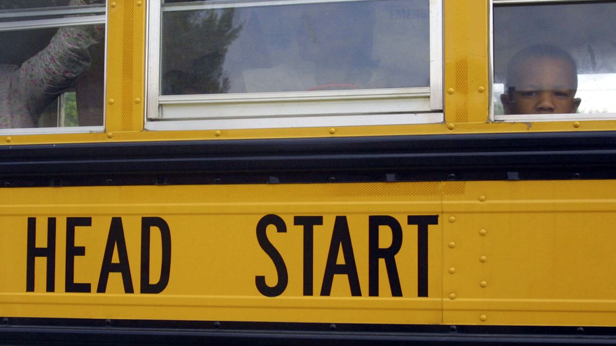 Young child looks out of window from a yellow school bus, which has the words Head Start printed on the side.
