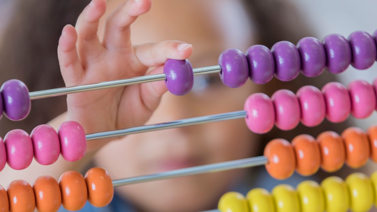 A young student's hand moves beads on a colorful counting abacus. The focus is on the abacus.