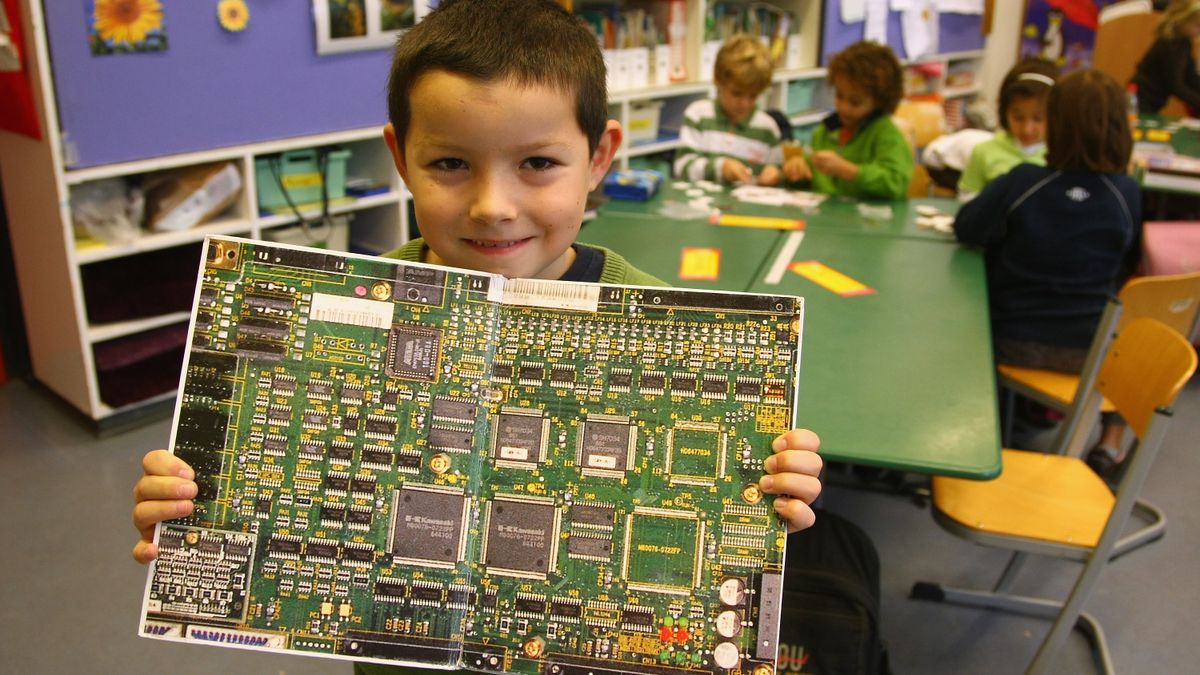 An 2nd-grade boy holds up a photo of a circuit board in a book about robots.