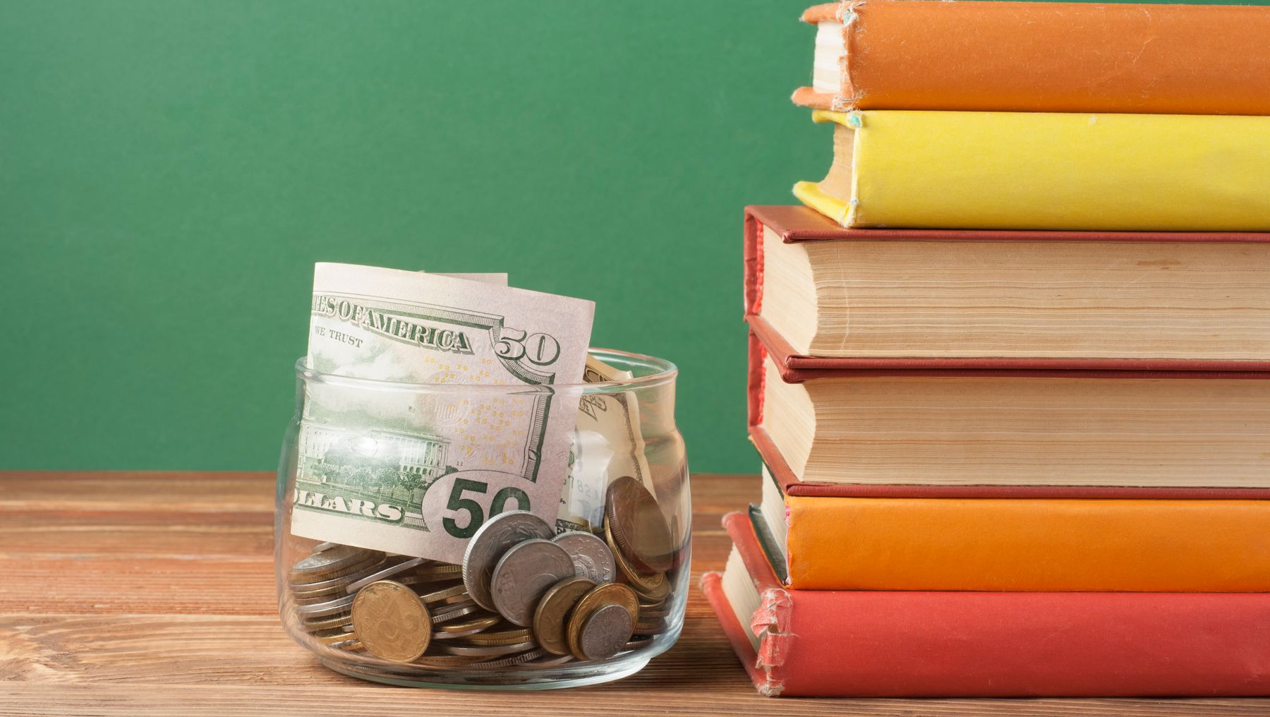 A jar of cash sits next to a stack of books on a teacher's desk.