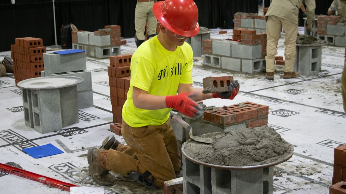 A person in a hardhat kneels, laying bricks.