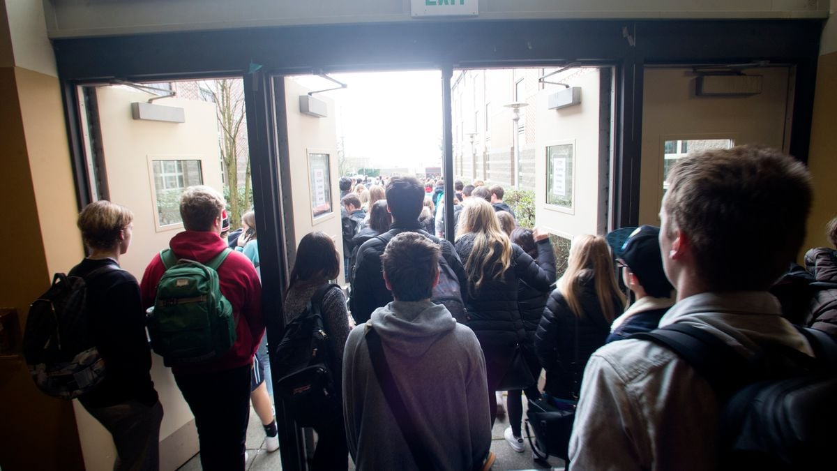 A group of students walk outside of a double set of doors in a school building.