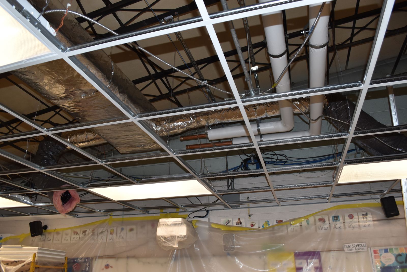 An exposed school classroom ceiling showing snow copper tubing for HVAC.